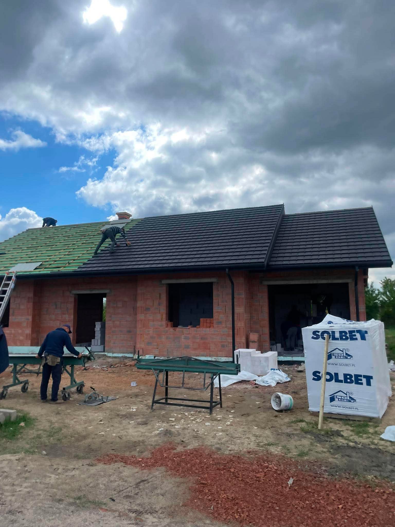 Dekarze kryją dach parterowego domu z czerwonych pustaków ceramicznych w stanie surowym