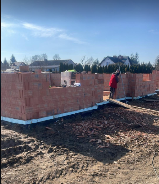 Pracownik przy murowaniu ścian z pustaków ceramicznych na fundamencie domu